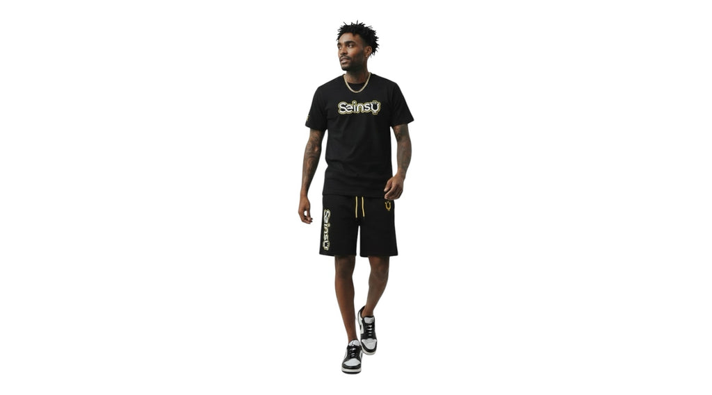 A man wearing a Seinsu Global black matching set with gold graphic t-shirt and drawstring shorts on a white background.
