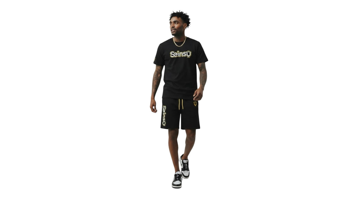 A man wearing a Seinsu Global black matching set with gold graphic t-shirt and drawstring shorts on a white background.