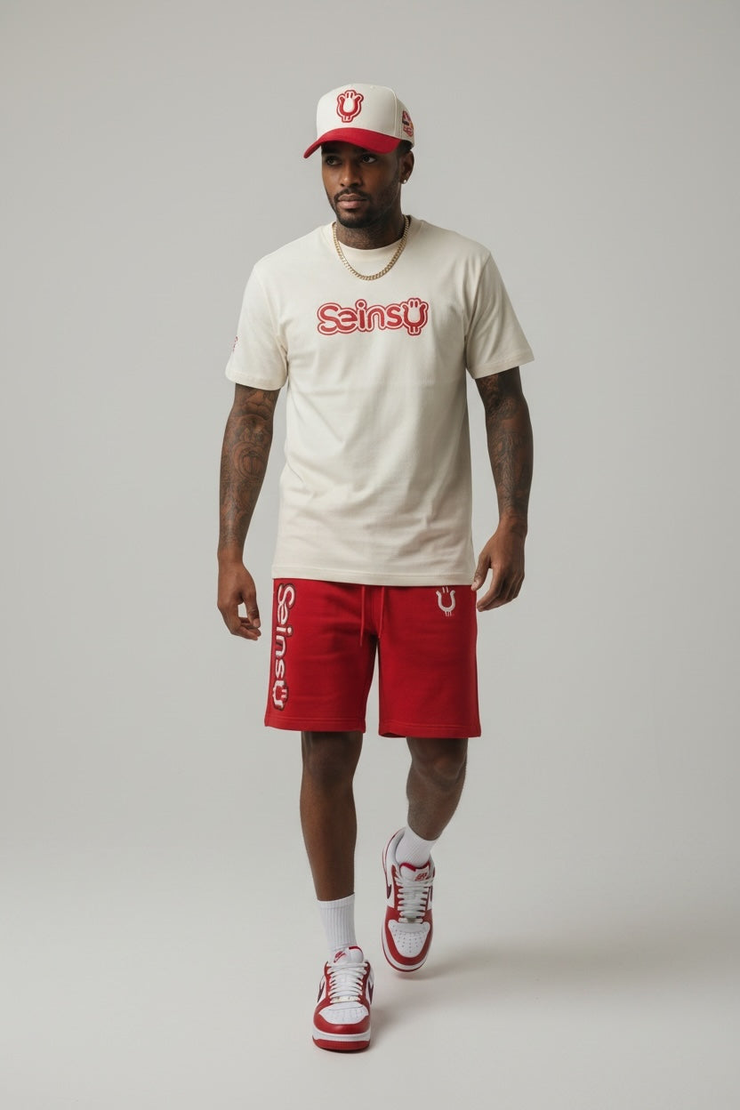 Model wearing Seinsu Global off-white graphic t-shirt, red athletic shorts, and matching cap on a grey background.